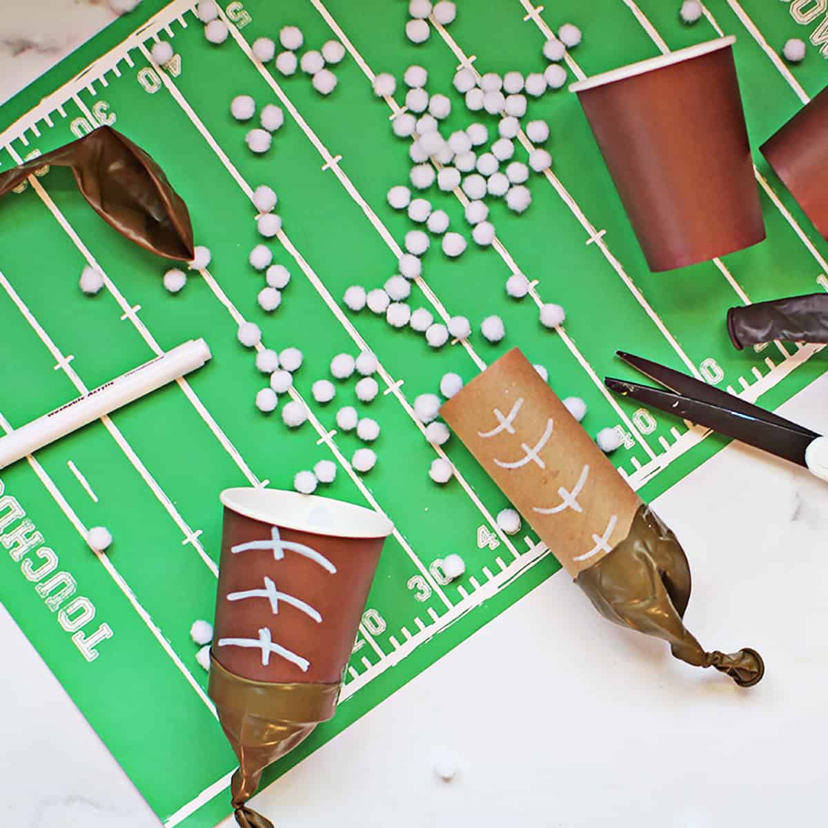 pom pom shooters made with brown cups and brown balloons to look like footballs on a football field placemat.