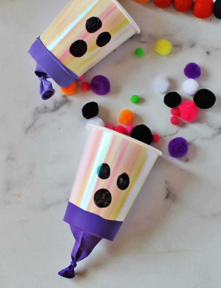 cup with a balloon wrapped around the bottom to shoot out pom poms and decorated to look like a ghost.