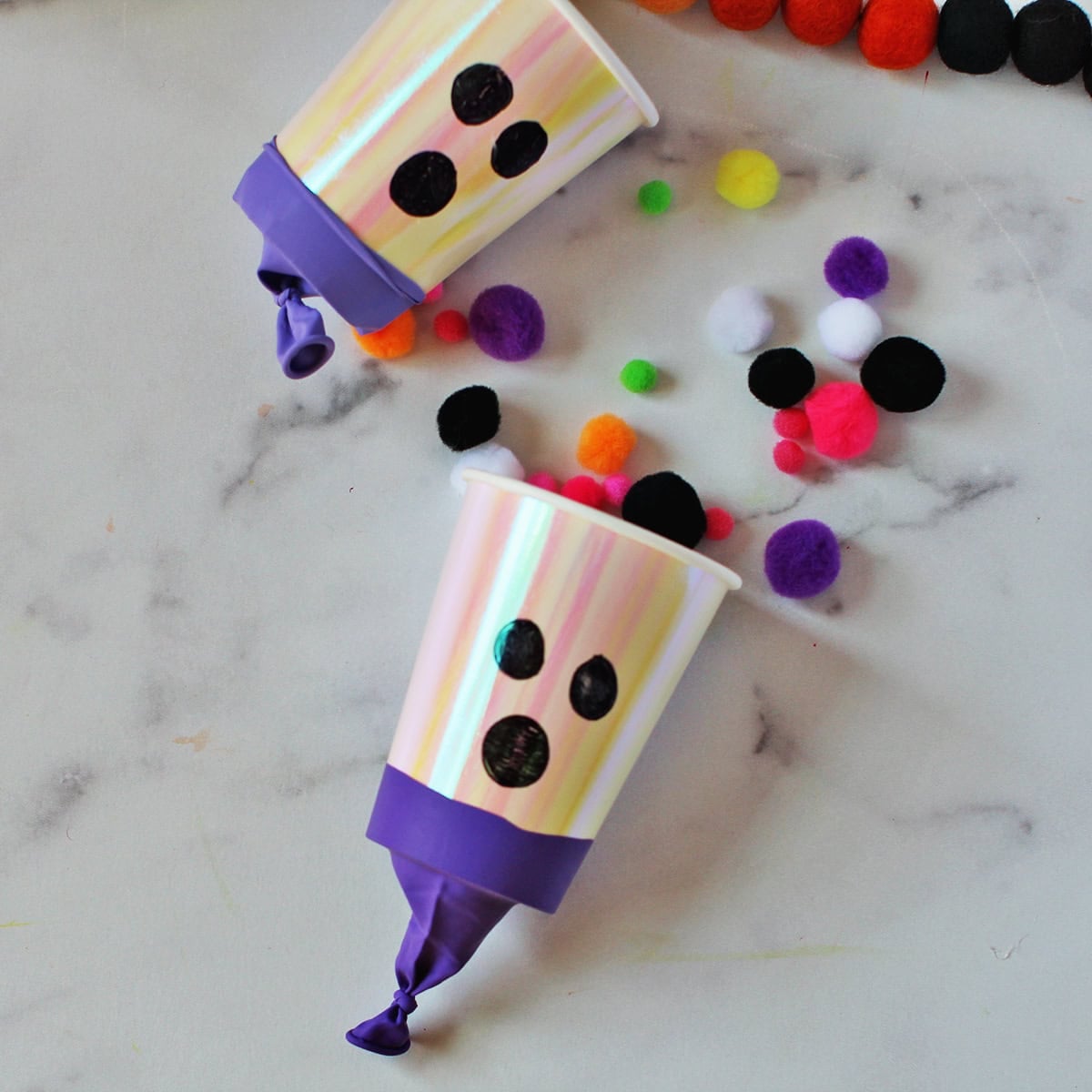cup with a balloon wrapped around the bottom to shoot out pom poms and decorated to look like a ghost.