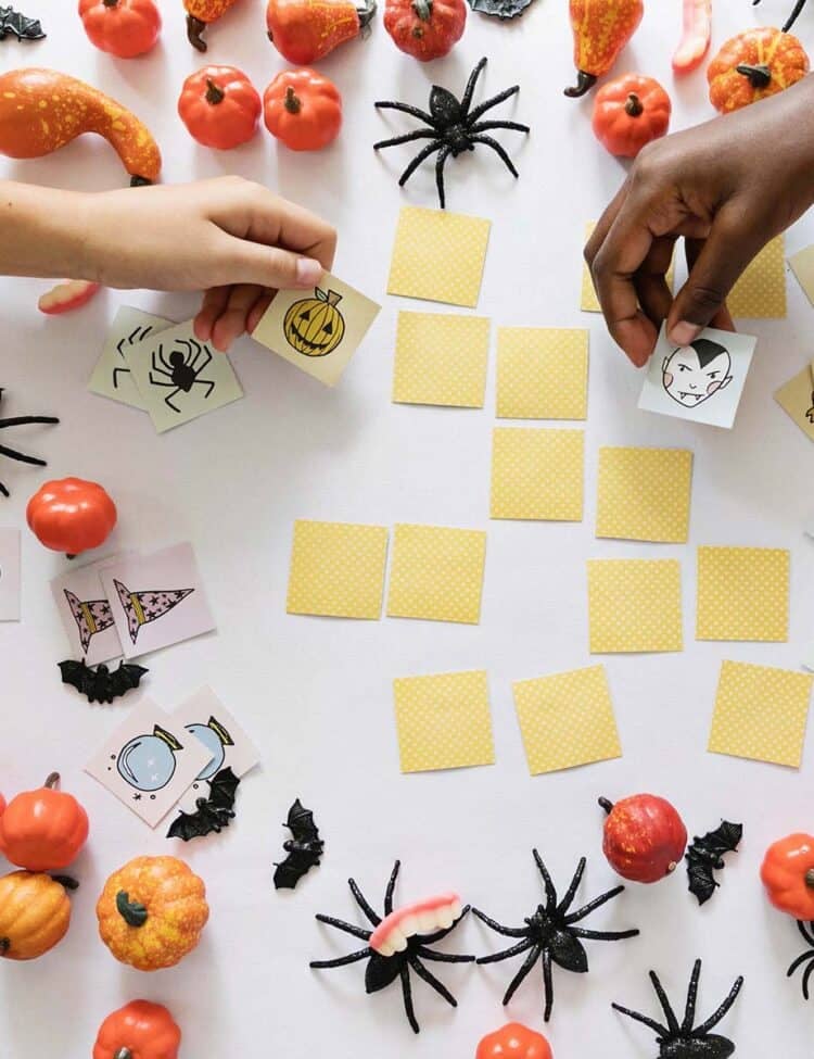 children's hands playing Halloween memory game on a table with toy spiders and pumpkins.