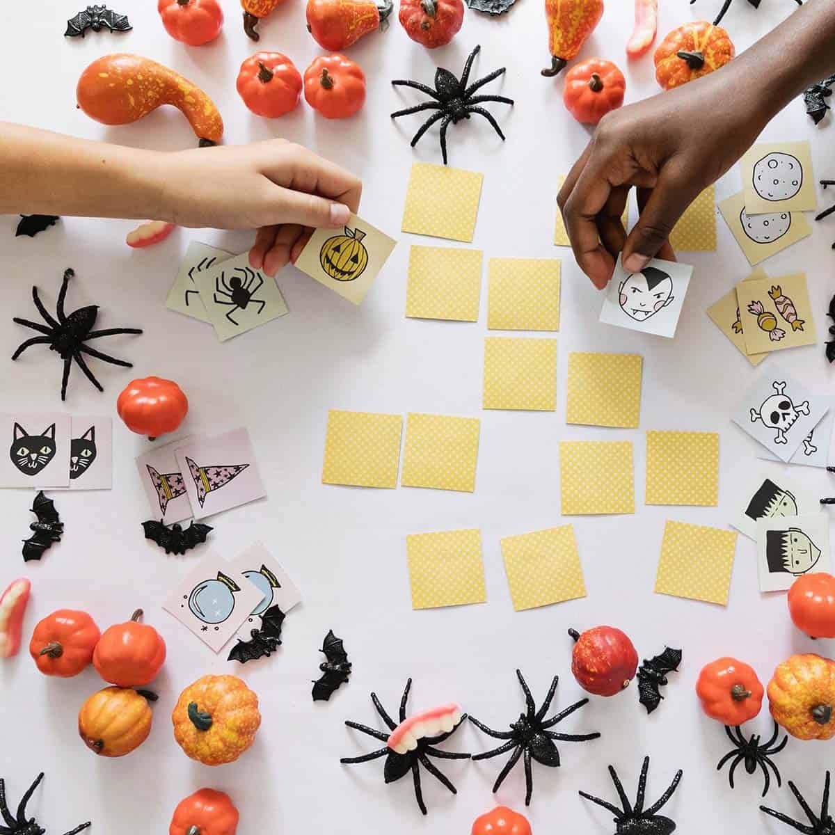 children's hands playing Halloween memory game on a table with toy spiders and pumpkins.