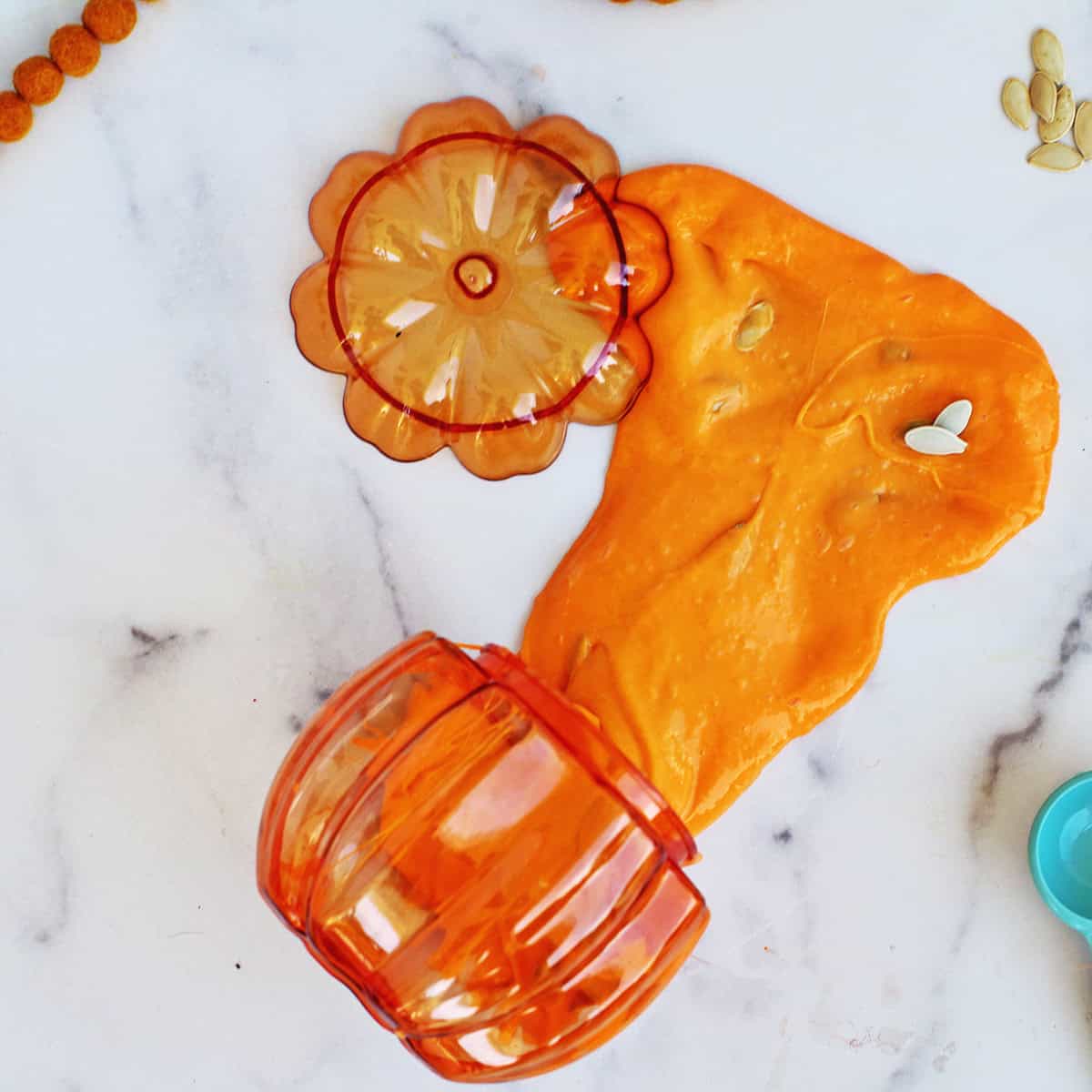 pumpkin slime with pumpkin seeds coming out of an orange plastic pumpkin container