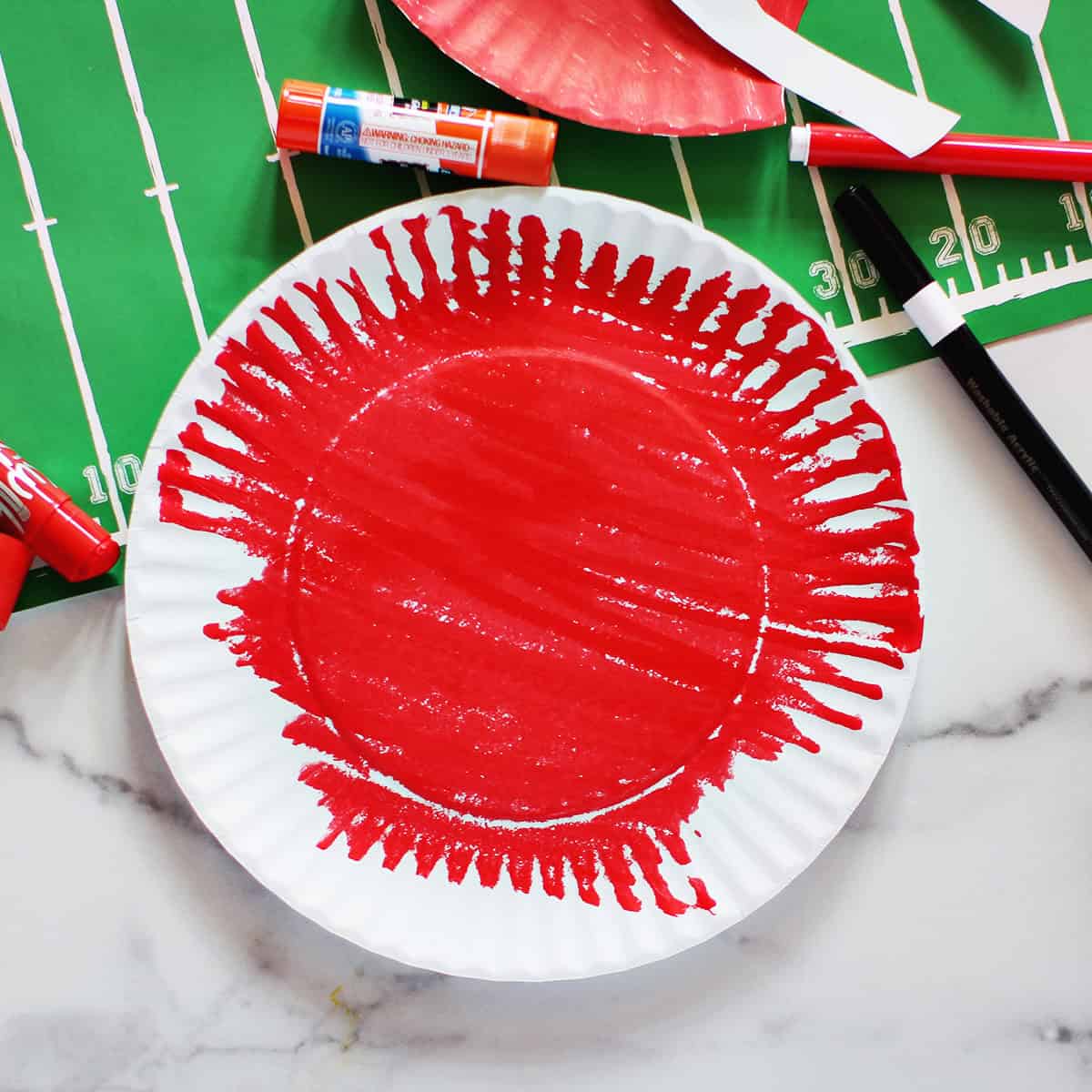 Paper plate being painted red with a paint pen.