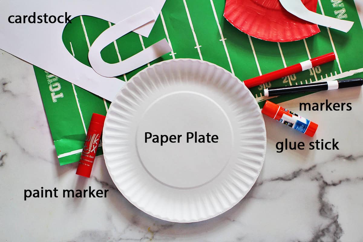 paper plate, paint marker, white paper, a glue stick and markers on a counter.
