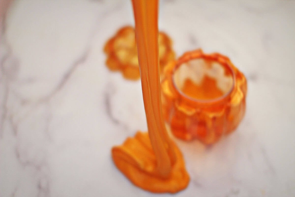 Orange slime being pulled upwards next to a plastic orange pumpkin container.