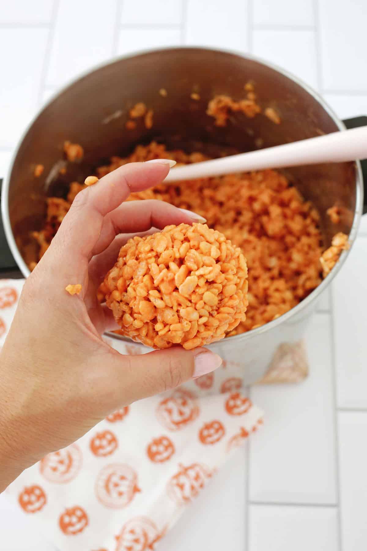 A hand holding rice krispie treats rolled into a ball shape.