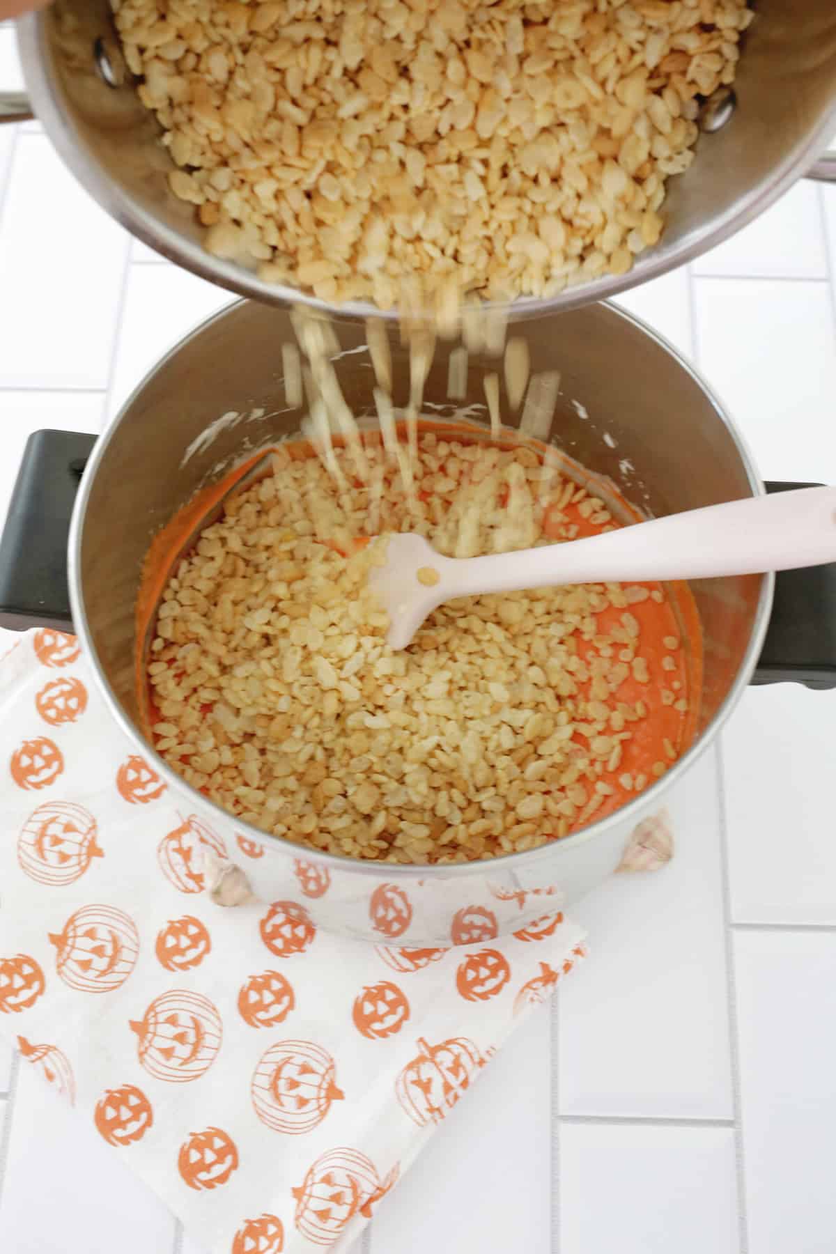 mixing melted marshmallow and rice krispies in a pot to make pumpkin shaped rice krispies treats.