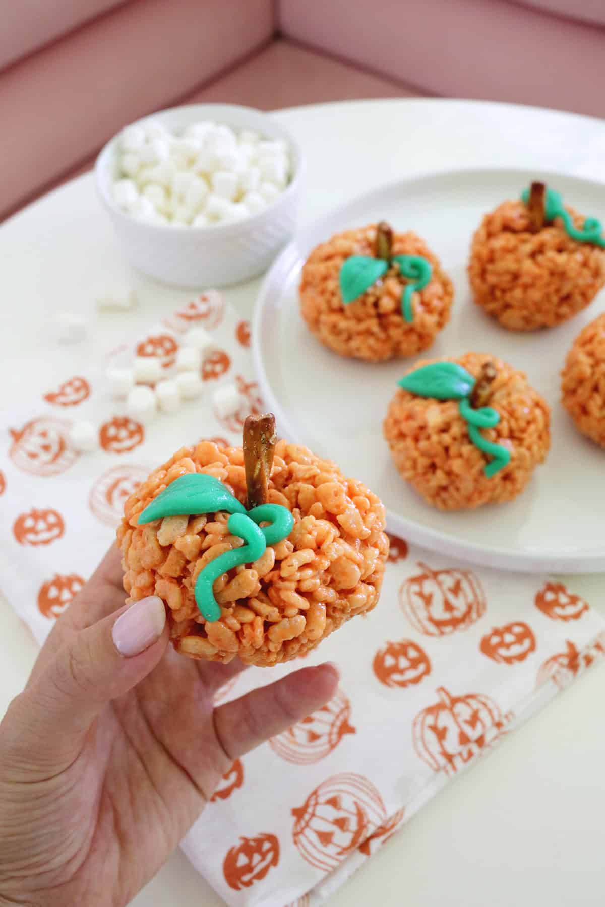 Hand holding a rice krispie treat in a pumpkin shape.