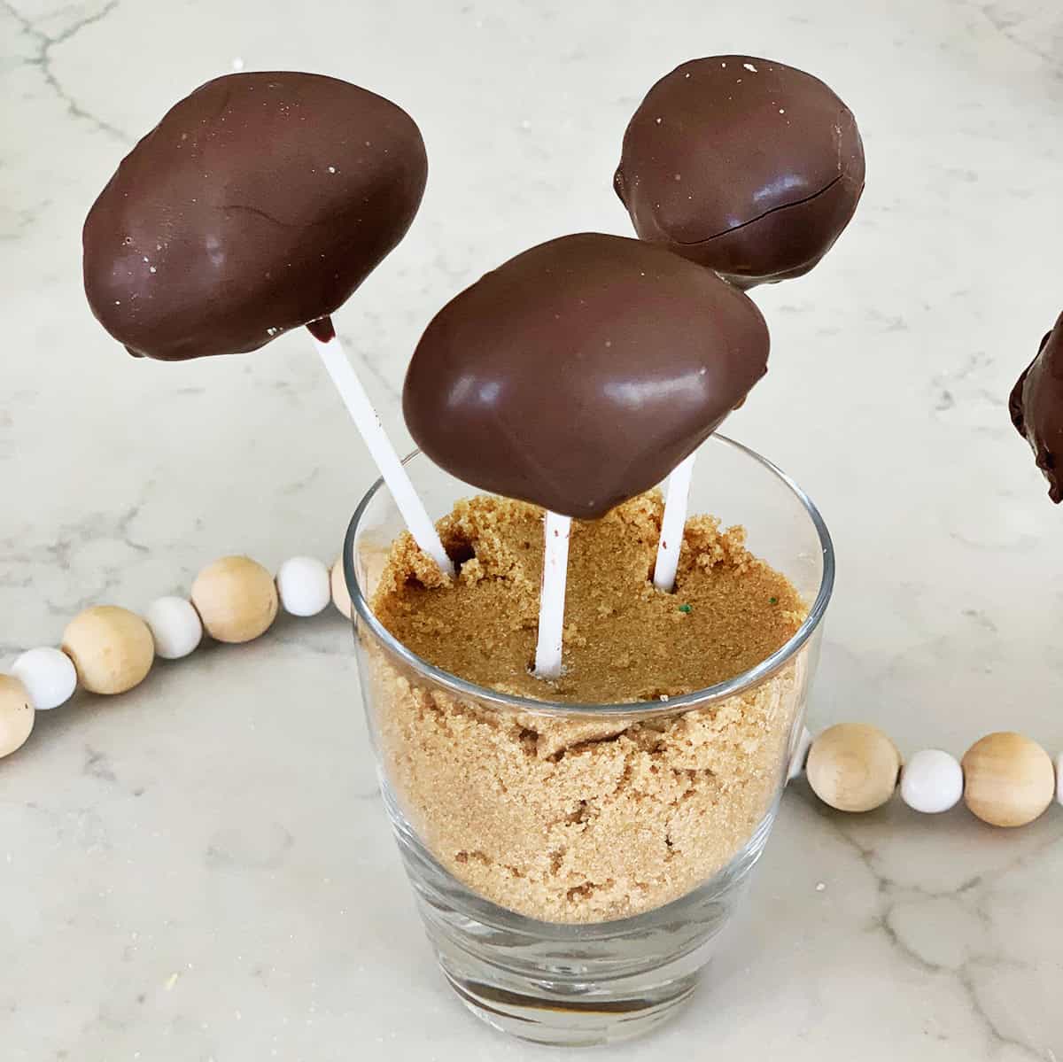 Cake pop in the shape of a football in a cup of brown sugar.