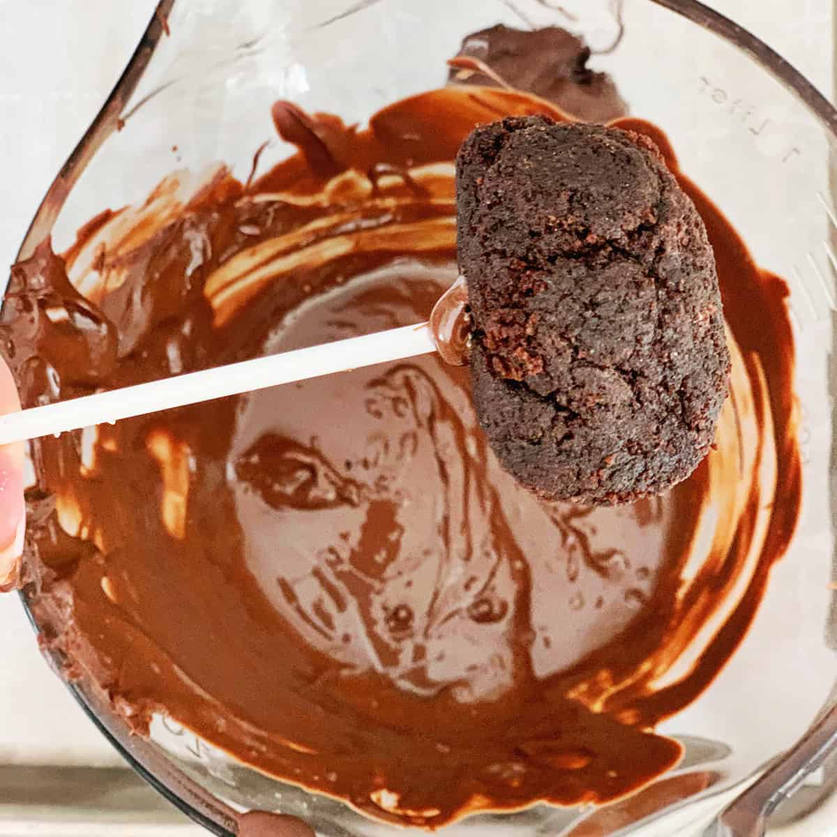 Cake pop stick with a chocolate cake ball on it being held over melted chocolate.