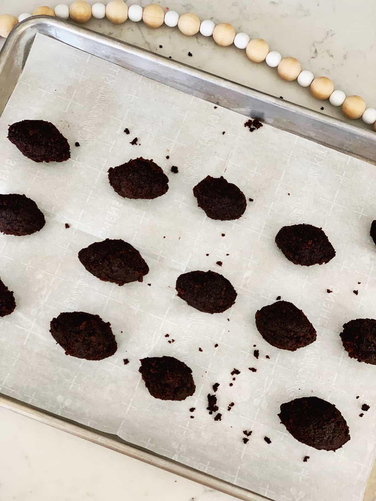 Chocolate cake balls rolled into football shapes on a baking sheet.