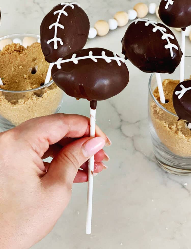 Hand holding a cake pop decorated to look like a football.