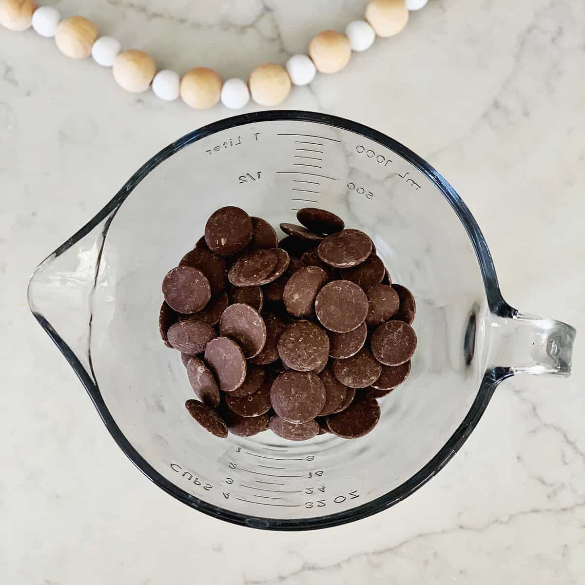 Chocolate melting wafers in a glass measuring dish.